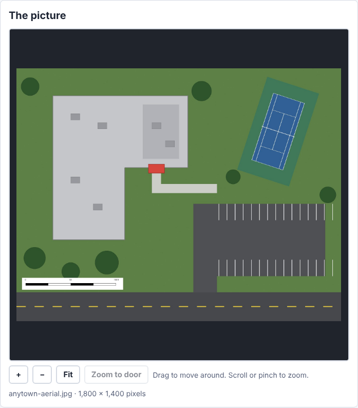 The Anytown sample picture: a school, a tennis court, a parking lot and a printed scale bar, with the zoom buttons under it